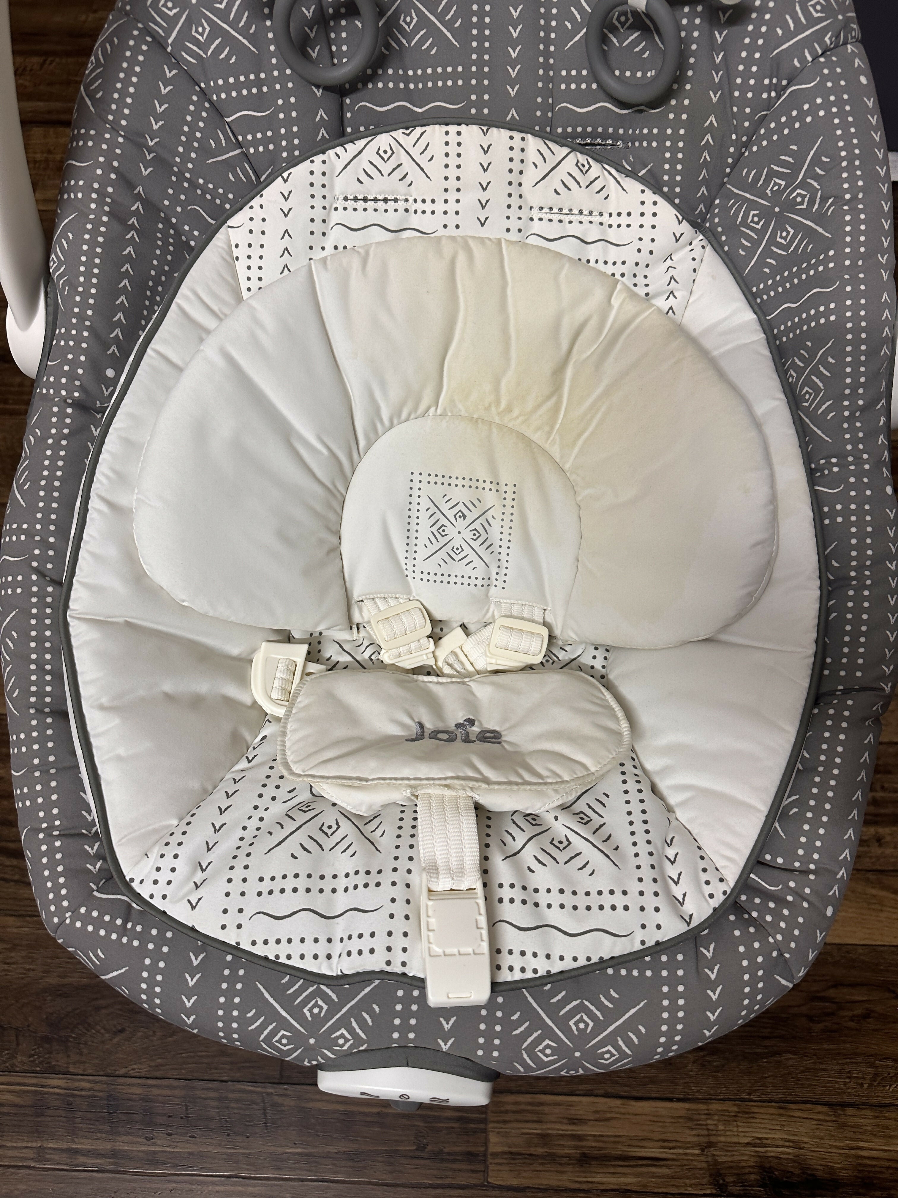 Baby bouncer with gray and white patterned cover on a wooden floor