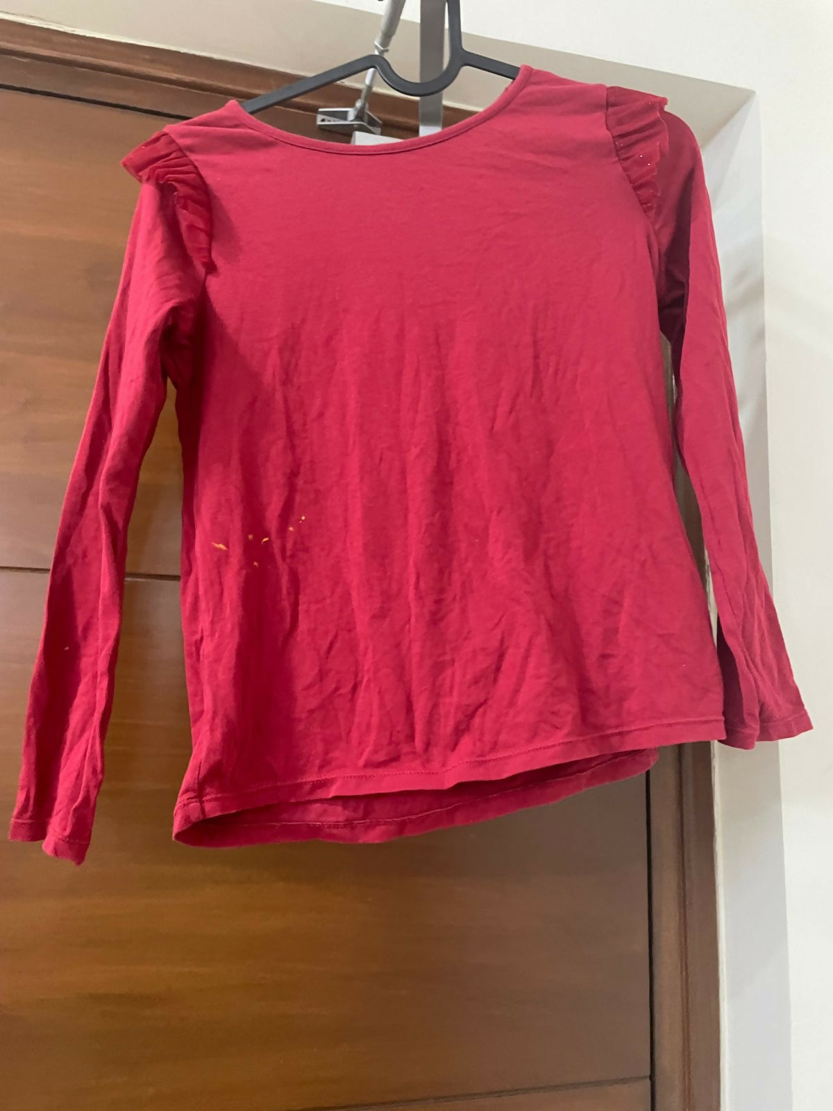 Red long-sleeve top on a hanger against a wooden door background