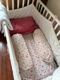 Crib with red and white bedding and pillows on a wooden floor.