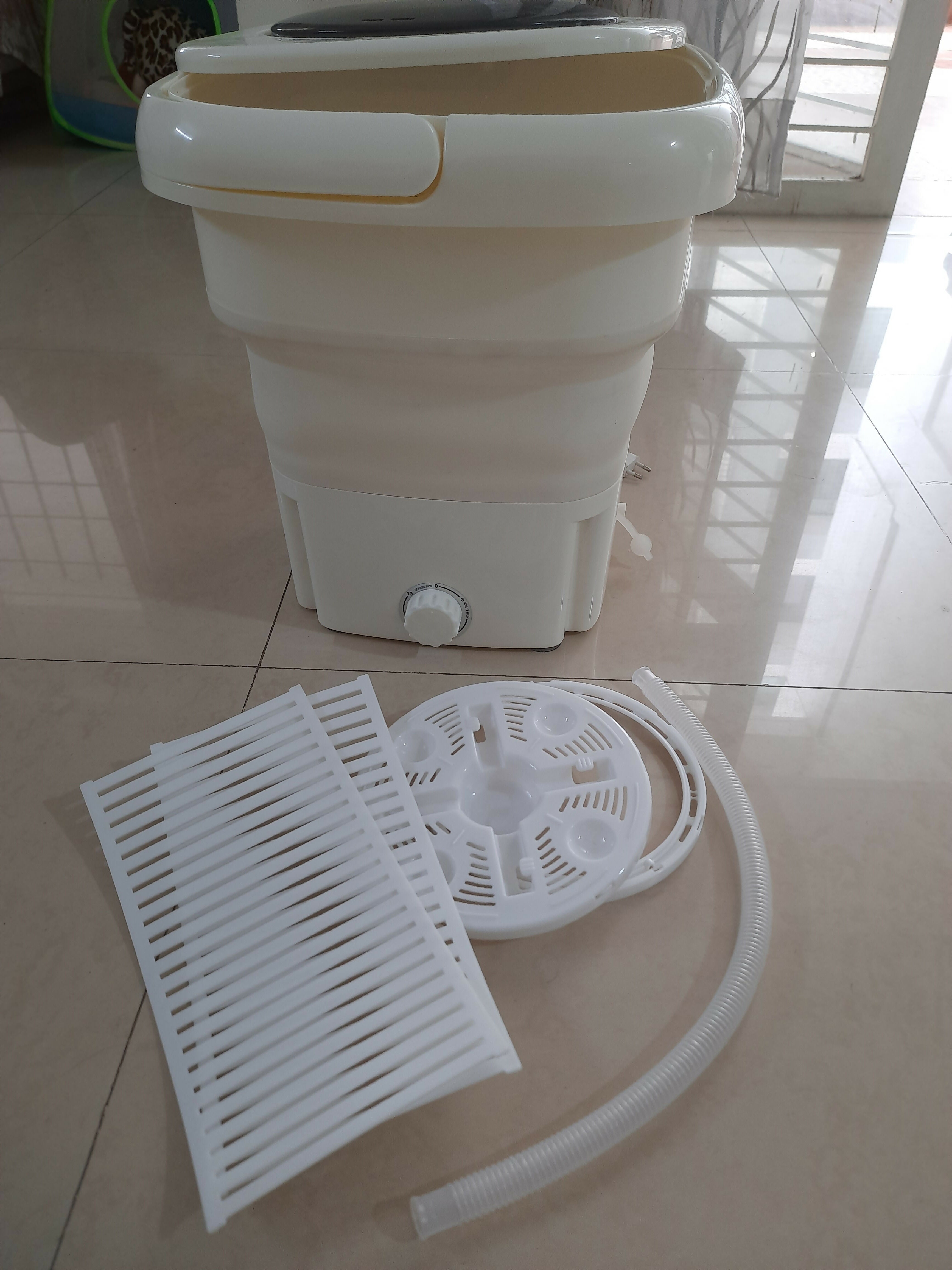 White collapsible washing machine with accessories on a tiled floor