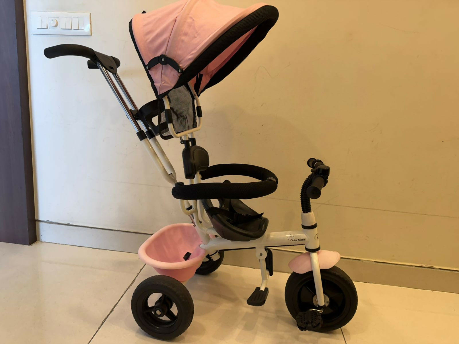 Pink and black baby tricycle on a light-colored floor.