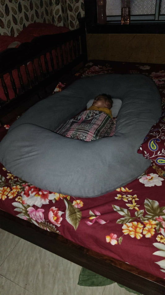 Person lying on a large gray pillow on a bed with floral bedding
