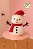 Snowman plush toy with a red scarf and hat on a pink stool against a pink wall.