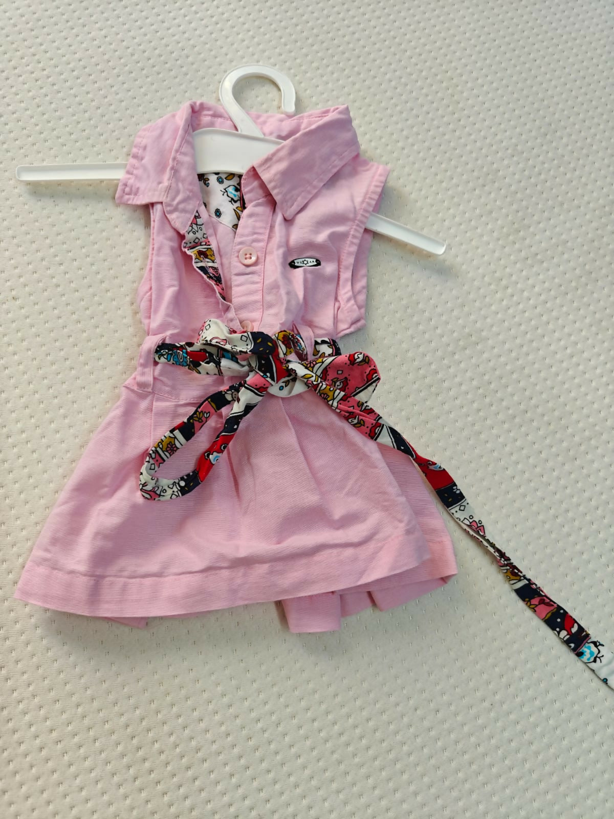Pink dress with a patterned belt on a white hanger against a light gray background