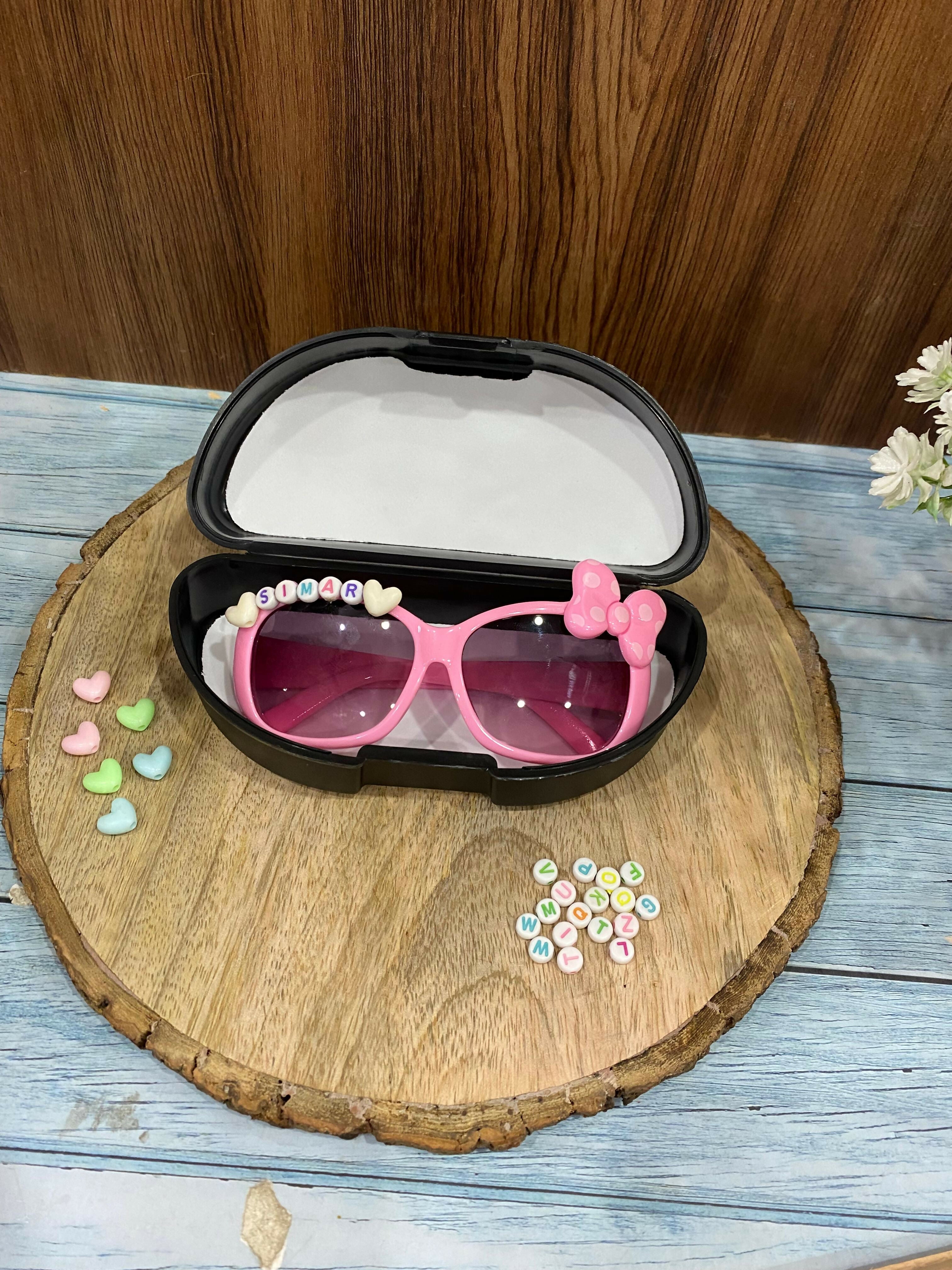 Pink sunglasses with decorative elements in a black case on a wooden surface.