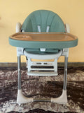 Green and brown high chair on a marble surface with a yellow wall background