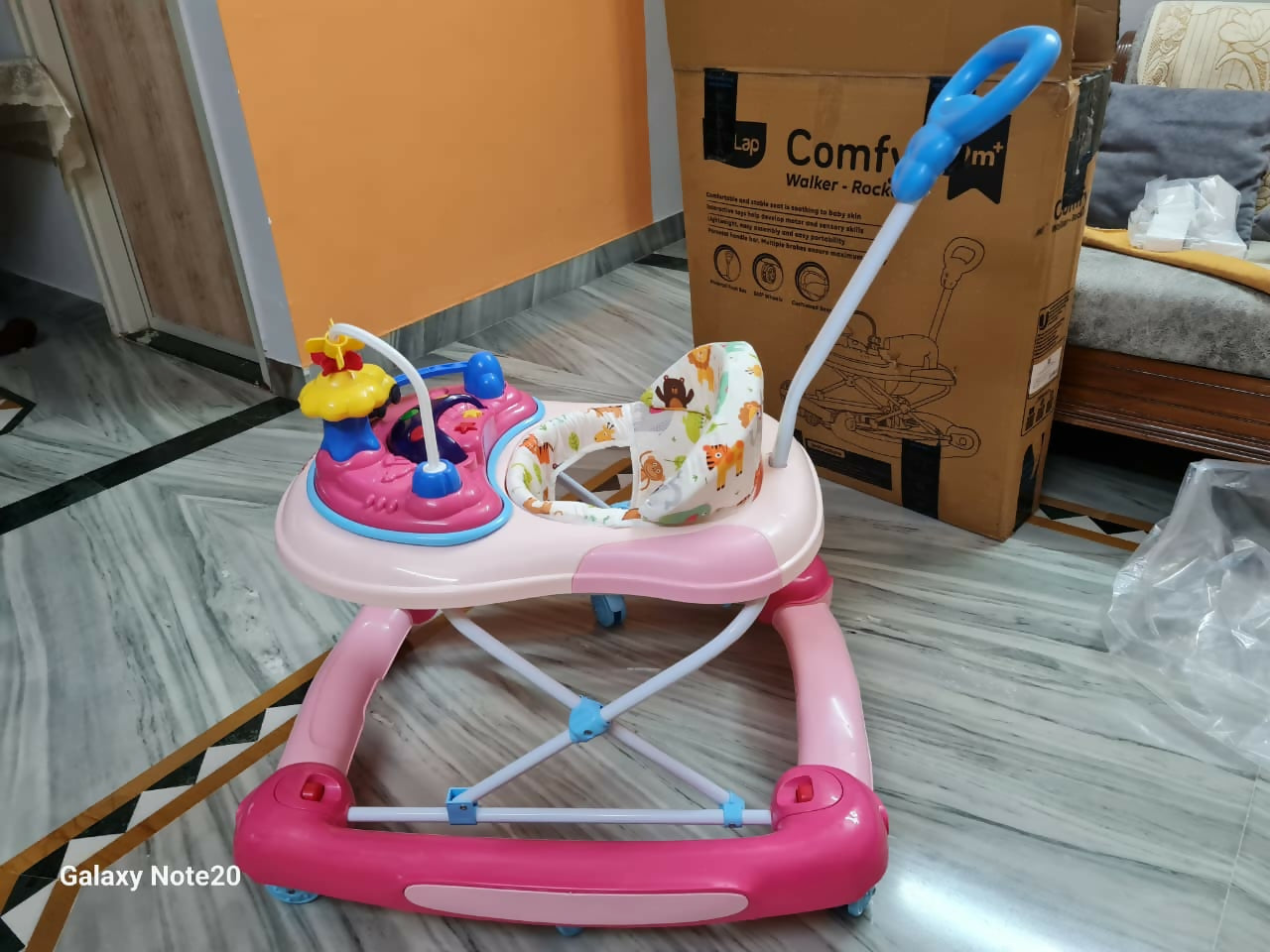 Pink baby walker on a floor with a cardboard box in the background