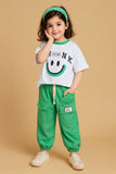 Child wearing a white t-shirt with a smiley face and green pants