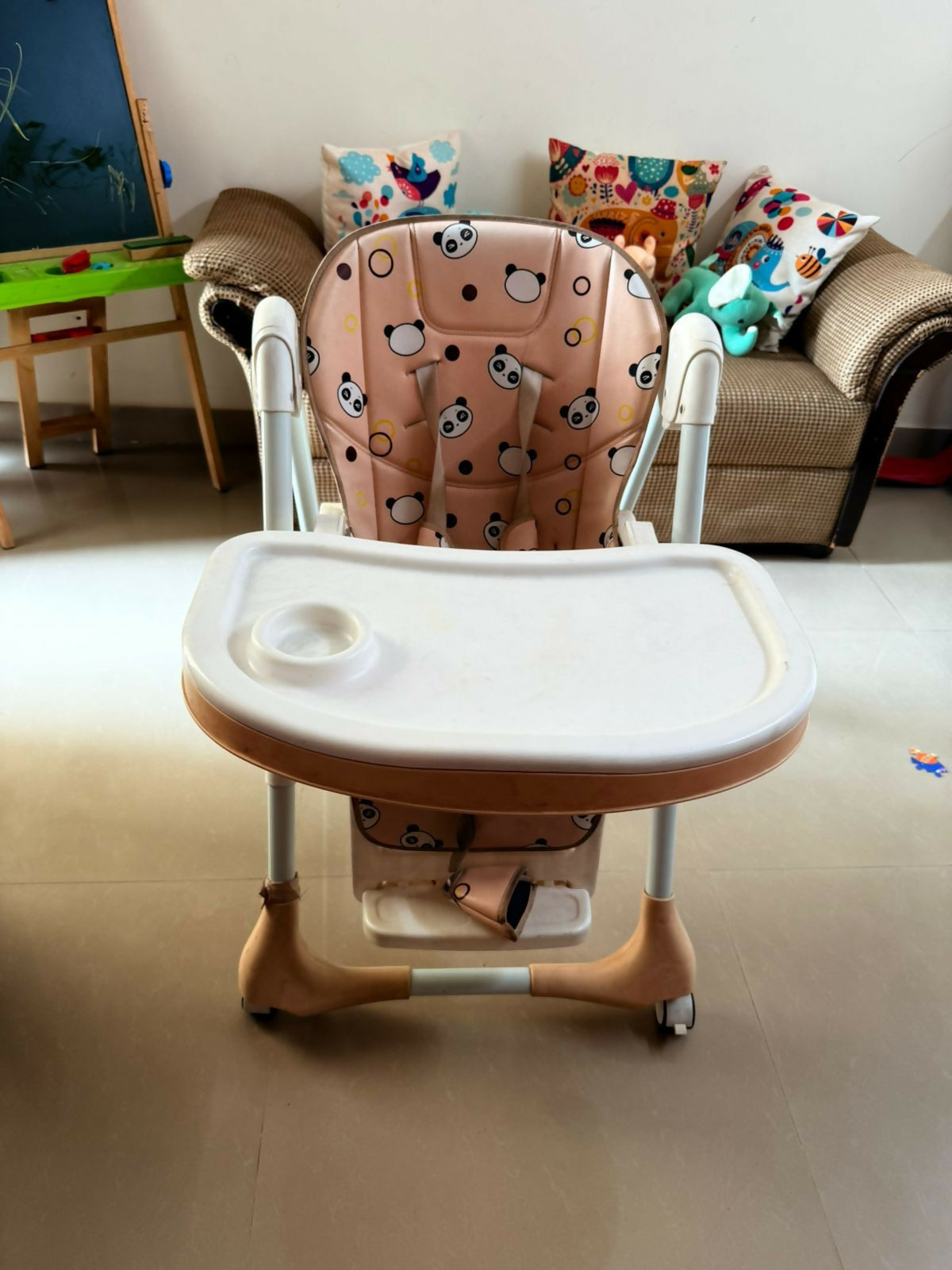 Children's high chair with cartoon-patterned cushion in a room with a couch and toys.