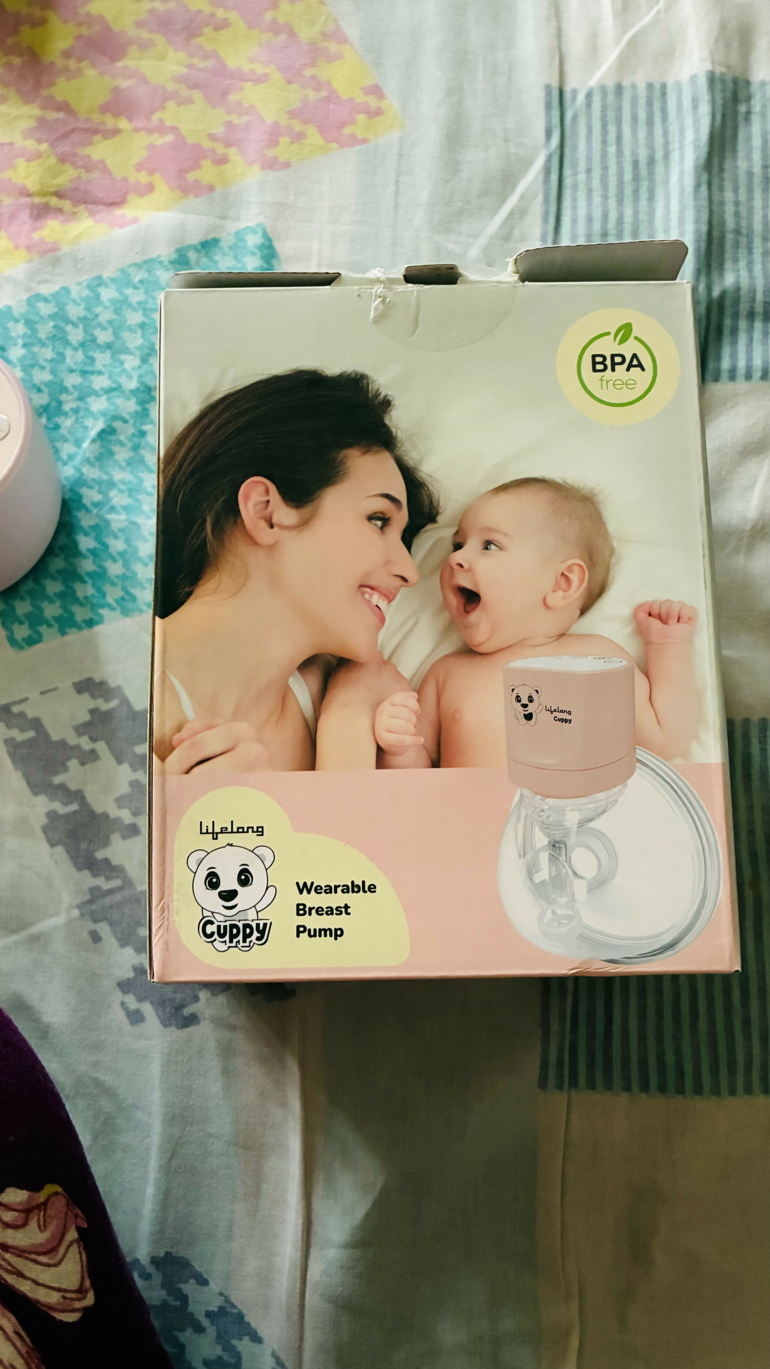 Product packaging for a wearable breast pump with a woman and baby illustration on a colorful background.