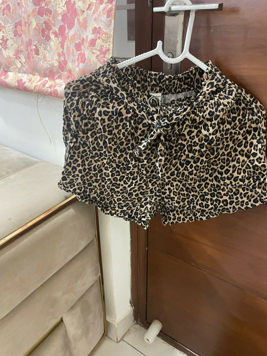 Leopard print shorts hanging on a hanger against a floral curtain background.