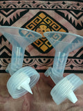 Two clear plastic funnels with white nozzles on a patterned fabric background