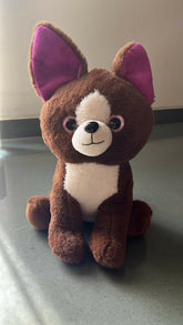 Plush toy dog with purple ears on a gray surface