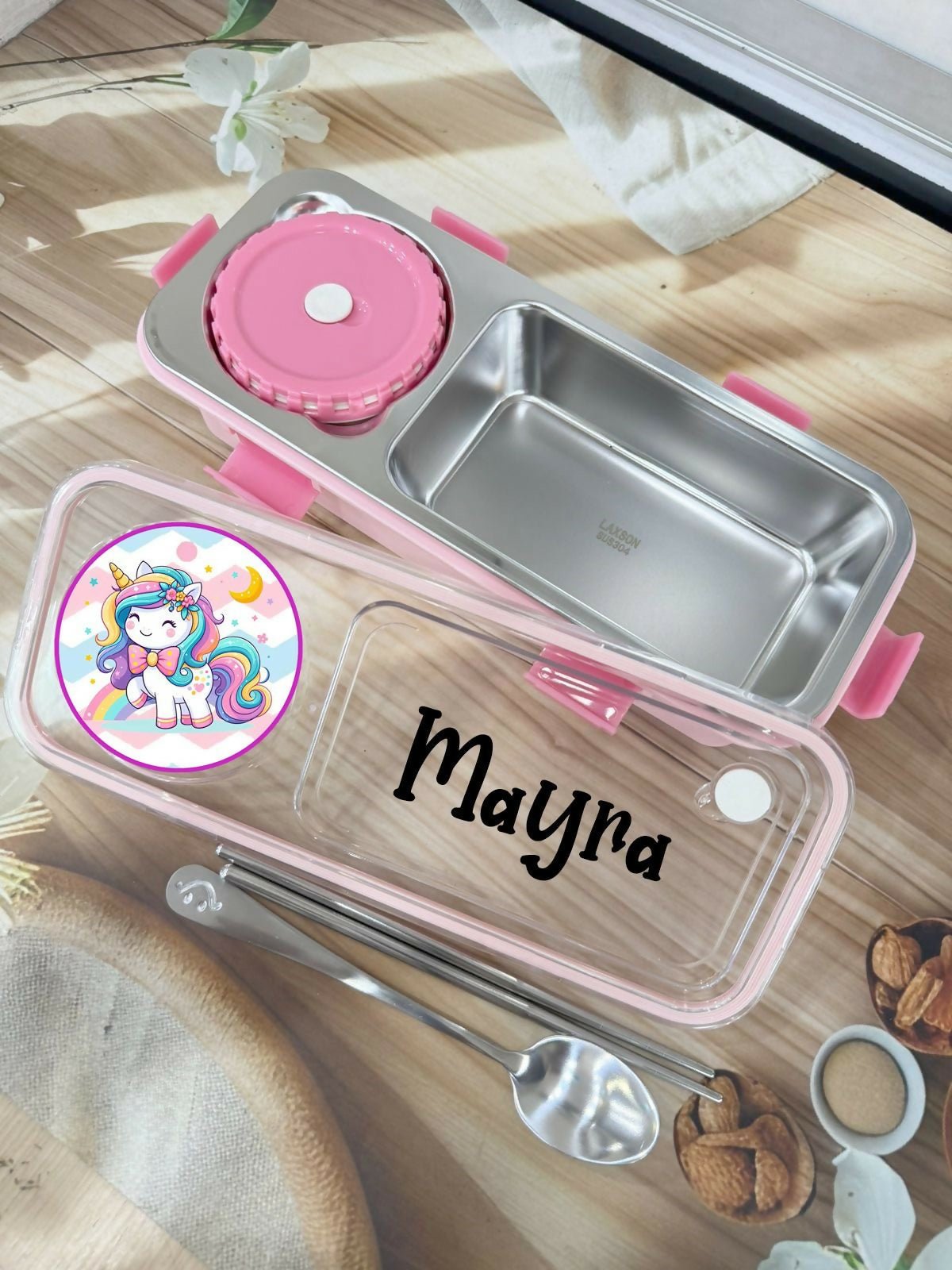 Stainless steel lunch box with pink accents and personalized name on a wooden surface.