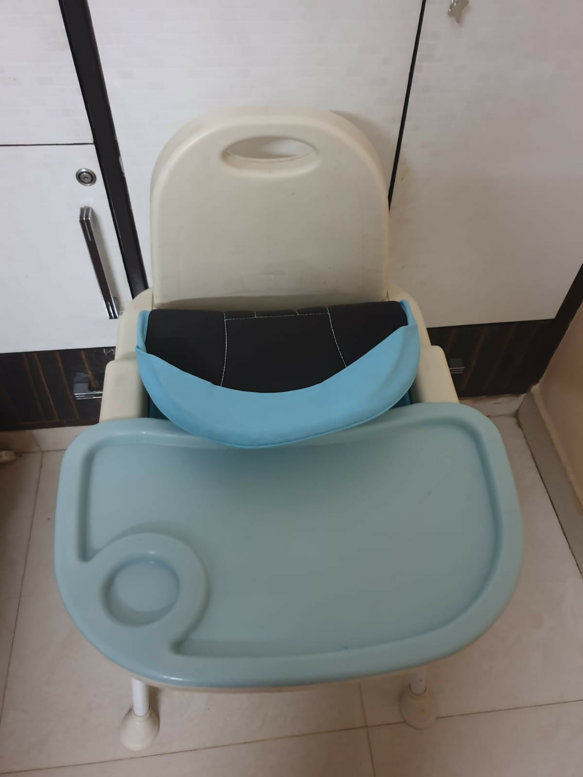 Children's chair with tray and seat cover on a tiled floor.