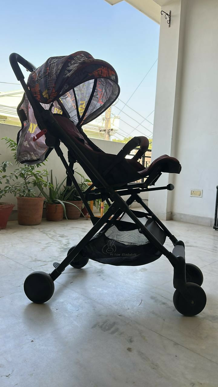 Black stroller with a colorful canopy on a concrete floor.