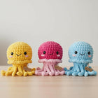 Three colorful crochet jellyfish toys on a wooden surface with a light gray background.