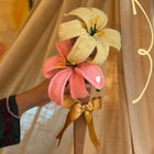 Decorative hair clip with pink and yellow flowers held by a hand against a curtain background