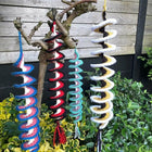 Colorful spiral wind chimes hanging from a tree branch outdoors.