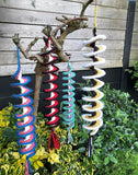 Colorful spiral wind chimes hanging from a tree branch outdoors.
