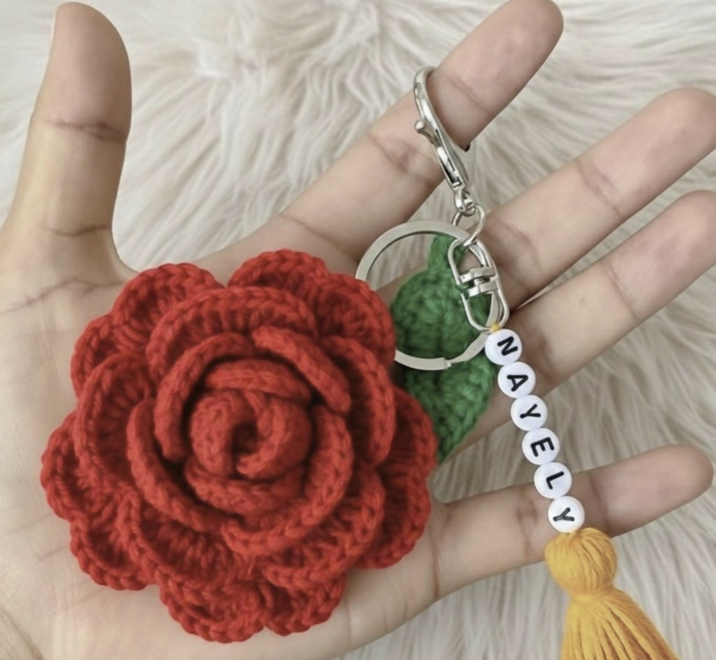 Hand holding a red crocheted flower keychain with a green leaf and yellow tasse