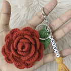Hand holding a red crocheted flower keychain with a green leaf and yellow tasse