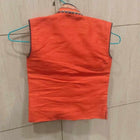 Orange sleeveless shirt on a hanger against a tiled wall