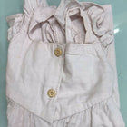 Folded light pink baby outfit with ruffled details on a light blue surface