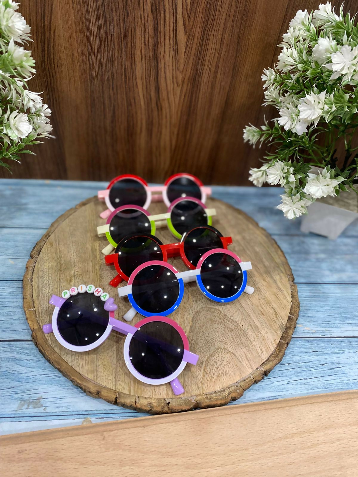 Colorful children's sunglasses on a wooden board with flowers in the background