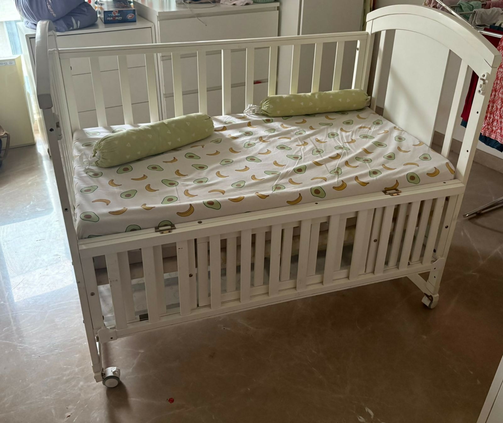 White crib with green and white bedding in a room setting