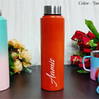 Orange water bottle with 'Aamus' branding on a wooden surface with flowers and other items.