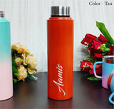 Orange water bottle with 'Aamus' branding on a wooden surface with flowers and other items.