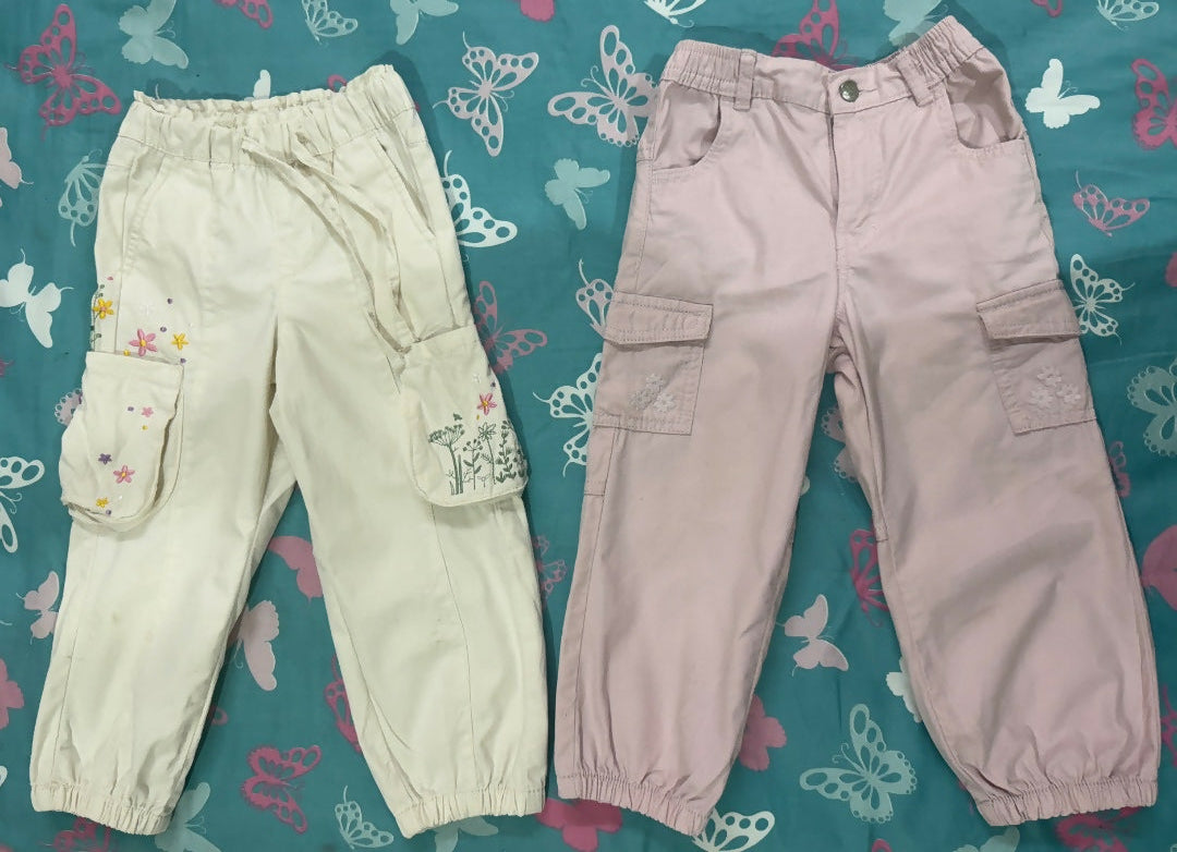 Two pairs of pants, one light green and one pink, on a blue fabric background with butterfly patterns.