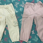 Two pairs of pants, one light green and one pink, on a blue fabric background with butterfly patterns.