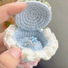 Crocheted ring holder with a blue ring inside, held by a hand against a blurred background.