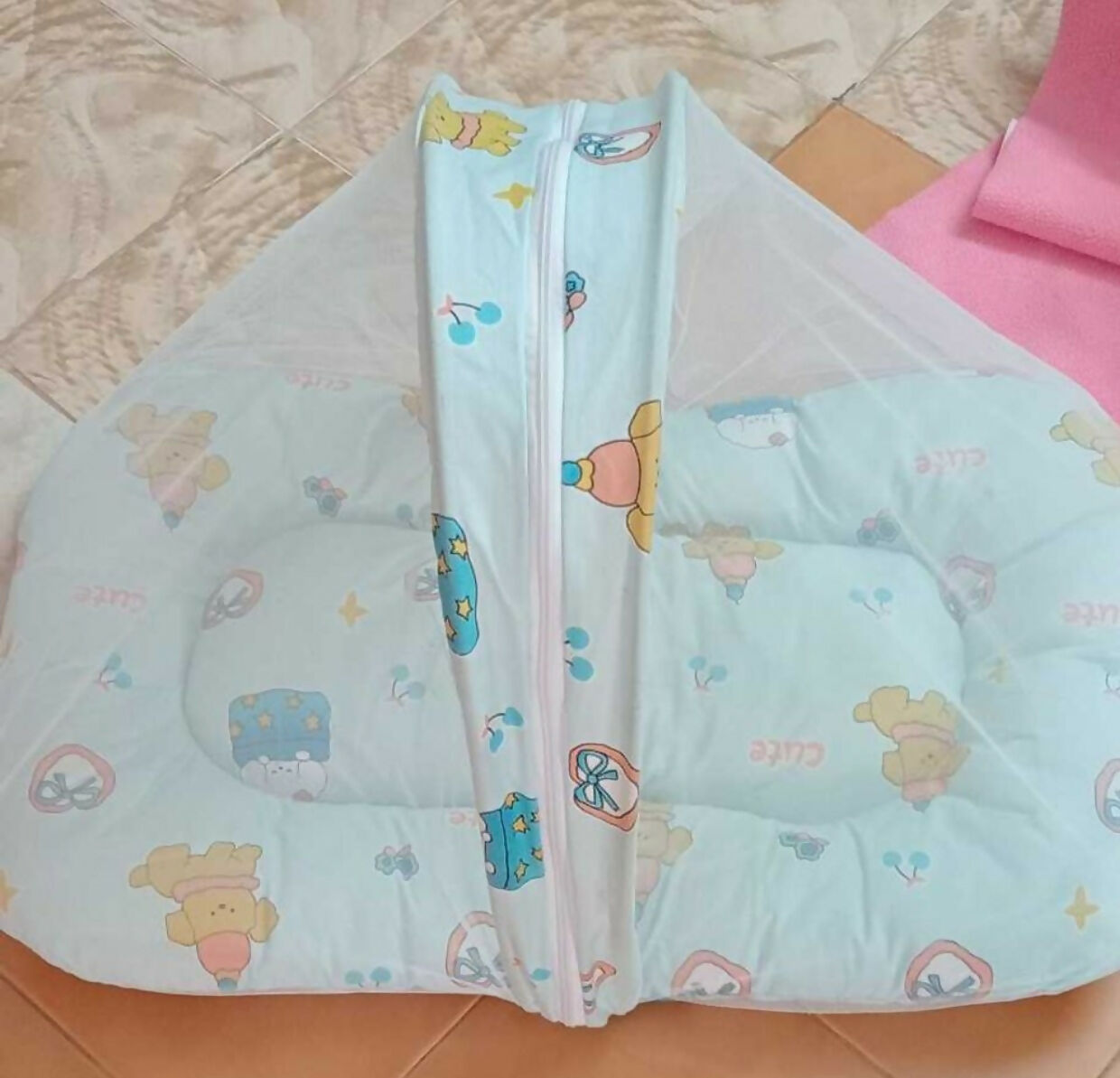 Light blue baby pillow with cartoon designs on a tiled floor
