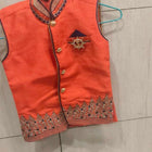 Orange embroidered vest on a hanger against a tiled wall background