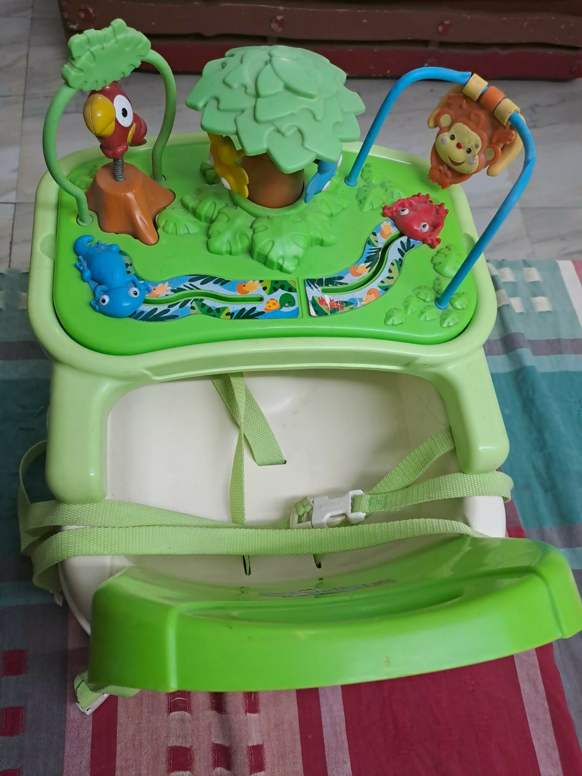 Green baby swing with colorful animals and toys on a checkered floor.
