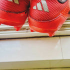 Red Adidas shoes with cleats on a tiled floor