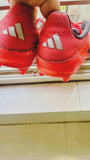 Red Adidas shoes with cleats on a tiled floor