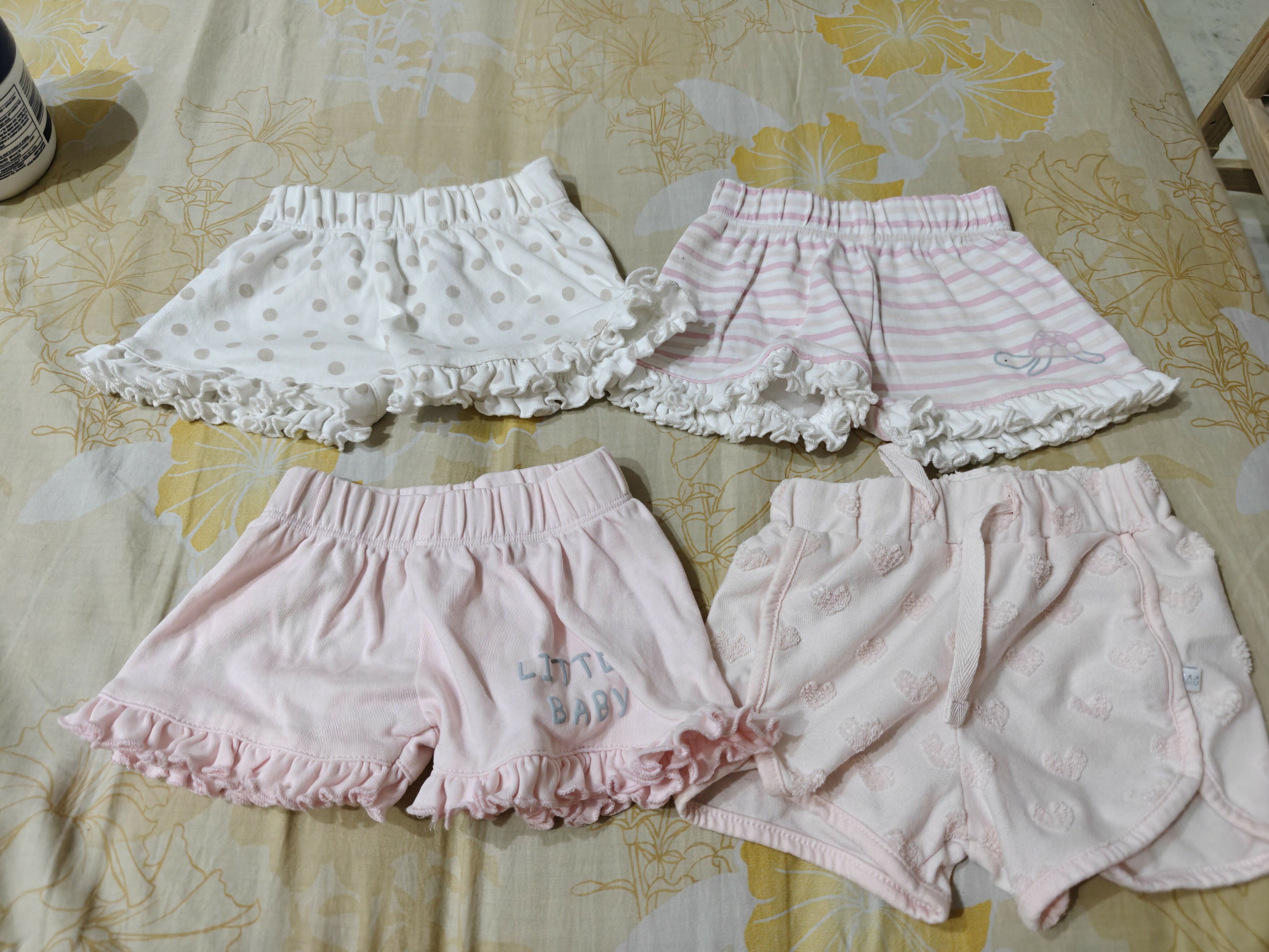 Four pairs of children's shorts on a floral-patterned bedspread.
