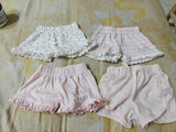 Four pairs of children's shorts on a floral-patterned bedspread.