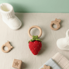 Strawberry-shaped teething ring with wooden rings and baby booties on a light surface.