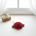 Red rose-shaped keychain on a white surface with a 'handmade with love' sign in the background.