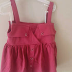 Pink dress with straps on a white hanger against a beige wall