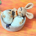 Knitted bunny toy with button details in a basket on a wooden surface