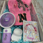 Pink cap with unicorn design, purple fan, white container, and notebook with 'Navya' branding in a box.