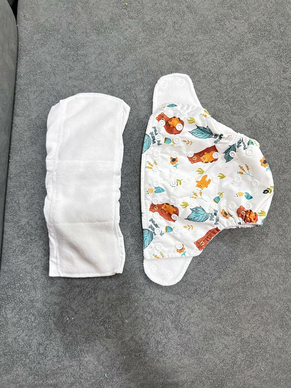 Two baby diapers on a gray surface, one plain and one with colorful designs.