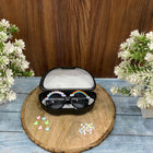Sunglasses with decorative elements in a case on a wooden coaster with flowers in the background