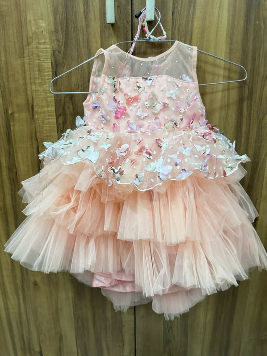 Pink children's dress with butterfly embellishments on a hanger against a wooden background